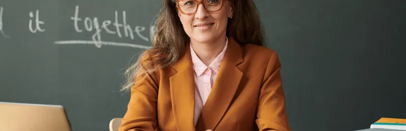 Head teacher sat at a desk in front of a chalk board